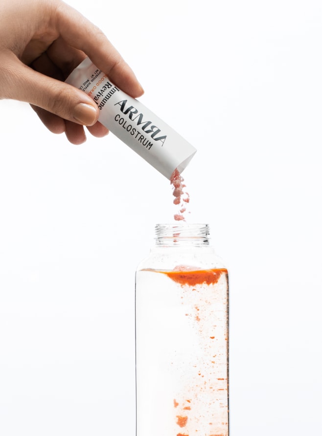 Hand pouring ARMRA colostrum sachet into water